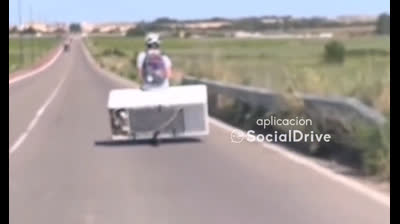 Un hombre lleva una nevera mientras conduce un patinete eléctrico